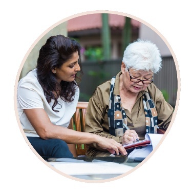 A person supporting an older person as they write on a document.