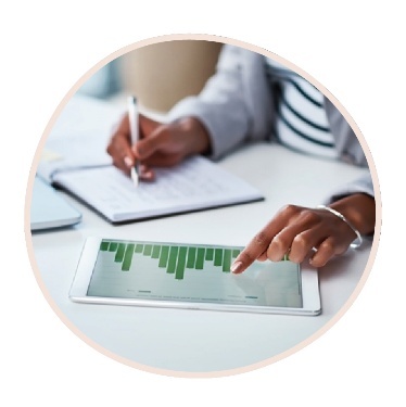 A person looking at research on a digital tablet. They are also writing on a document.